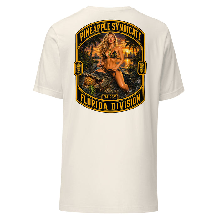 Pineapple Syndicate Florida Division tee featuring a blonde pinup riding an alligator through swamp water with an upside-down pineapple, sunset backdrop, and bold black-and-gold framing.